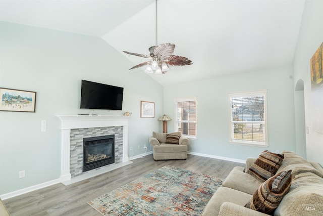 living room with lofted ceiling, ceiling fan, wood finished floors, a tile fireplace, and baseboards