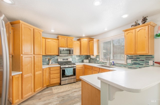 kitchen featuring appliances with stainless steel finishes, a peninsula, light countertops, light brown cabinetry, and a sink