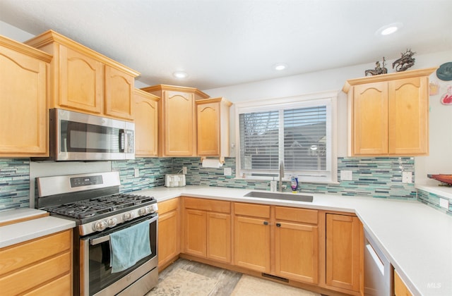 kitchen with stainless steel appliances, tasteful backsplash, light countertops, light brown cabinets, and a sink