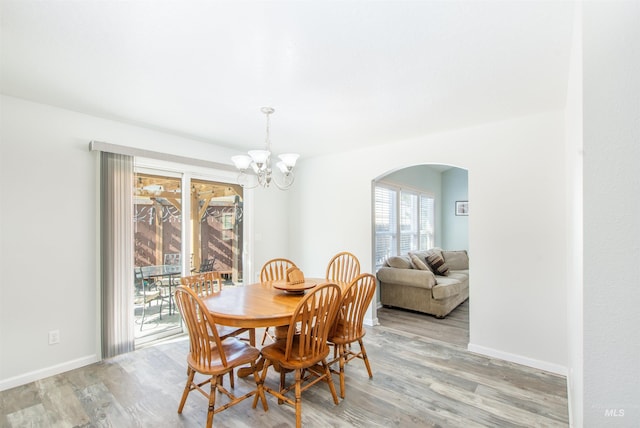 dining space with light wood-style floors, arched walkways, a notable chandelier, and baseboards