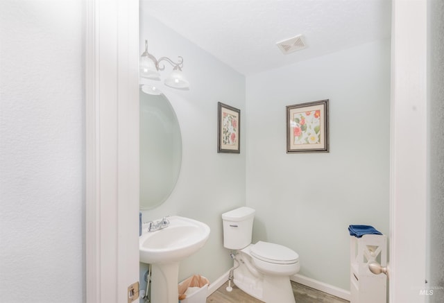 bathroom with baseboards, visible vents, toilet, and wood finished floors