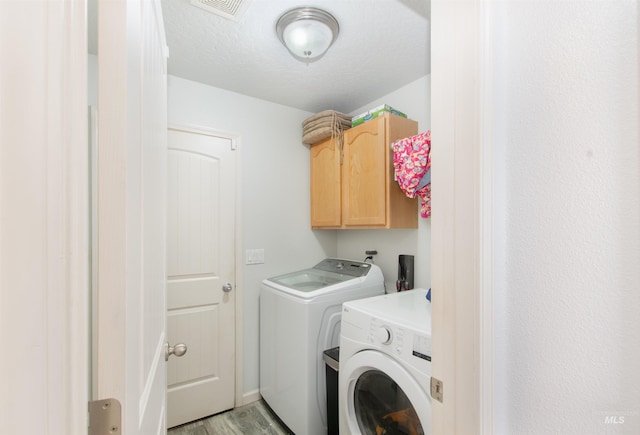 clothes washing area featuring a textured ceiling, visible vents, light wood-style floors, cabinet space, and washer and clothes dryer