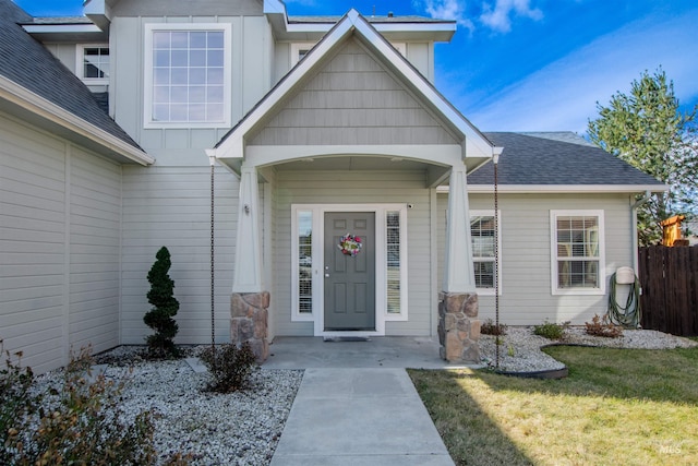 property entrance featuring a yard, a shingled roof, board and batten siding, and fence