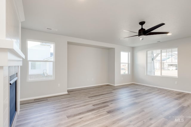 unfurnished living room with visible vents, light wood-style floors, baseboards, ceiling fan, and a tile fireplace