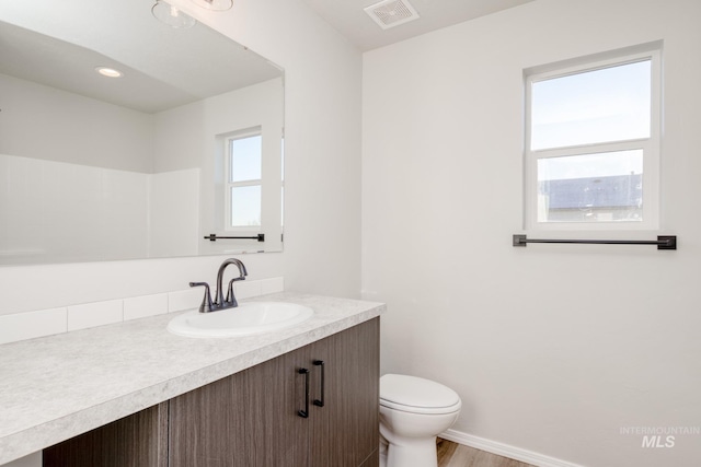 bathroom featuring visible vents, baseboards, toilet, wood finished floors, and vanity