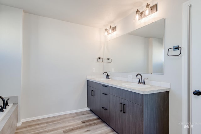 full bathroom featuring a sink, baseboards, wood finished floors, and double vanity