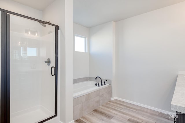 full bath featuring a bath, a shower stall, baseboards, and wood finished floors