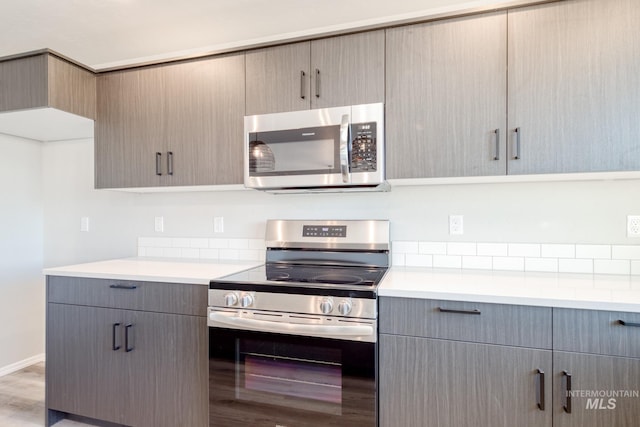 kitchen with light wood-type flooring, gray cabinets, stainless steel appliances, light countertops, and baseboards