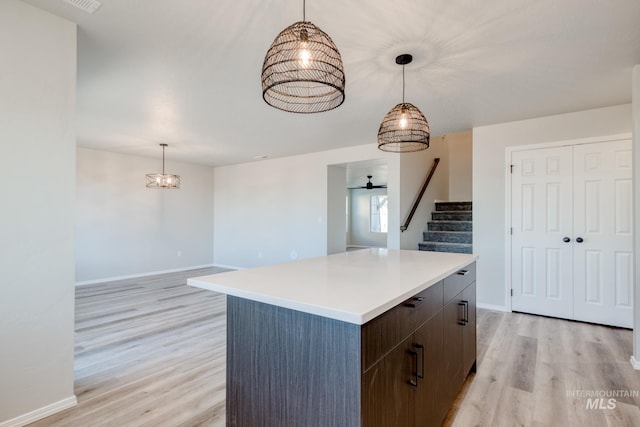 kitchen with decorative light fixtures, a kitchen island, light wood-style floors, light countertops, and baseboards