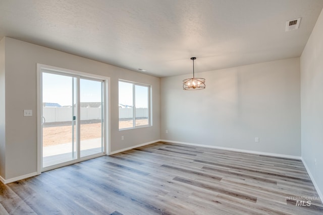 empty room featuring an inviting chandelier, light wood-style floors, visible vents, and baseboards