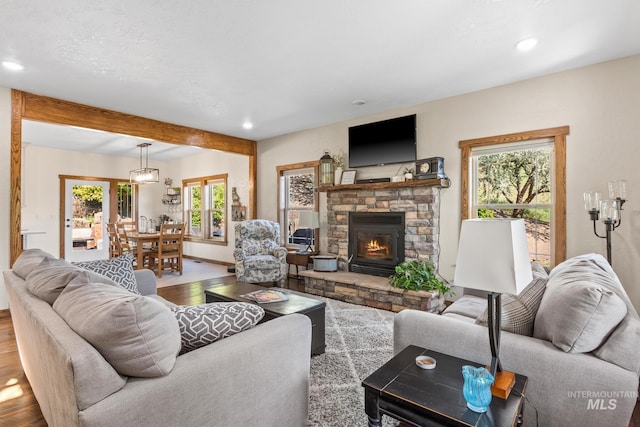 living area featuring wood finished floors, a stone fireplace, recessed lighting, beamed ceiling, and baseboards