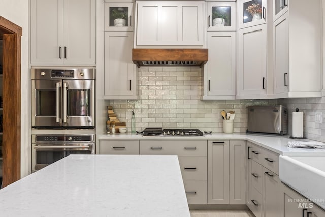 kitchen featuring stainless steel appliances, tasteful backsplash, glass insert cabinets, and light stone counters