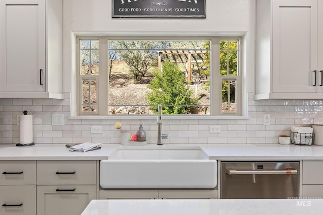 kitchen featuring stainless steel dishwasher, a sink, backsplash, white cabinets, and light stone countertops