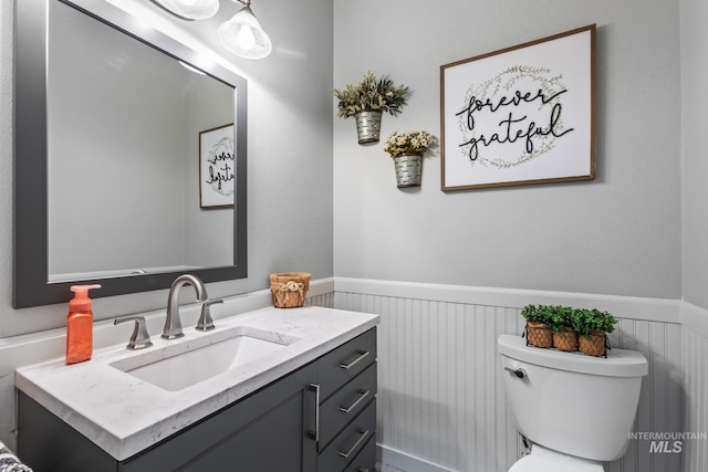 half bathroom featuring wainscoting, vanity, and toilet