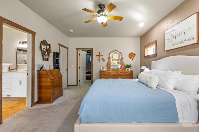 bedroom featuring light colored carpet, ensuite bath, a walk in closet, a ceiling fan, and a closet