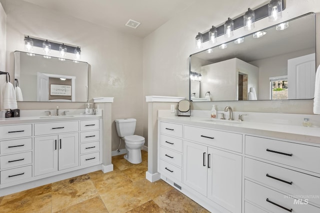 bathroom with toilet, two vanities, and baseboards