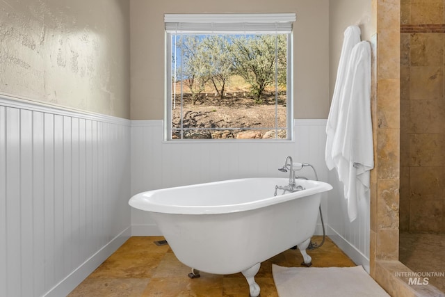 bathroom featuring a wainscoted wall, a soaking tub, and a tile shower