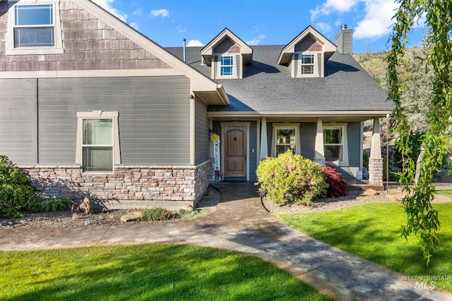 craftsman-style house featuring stone siding, a chimney, a front yard, a porch, and roof with shingles