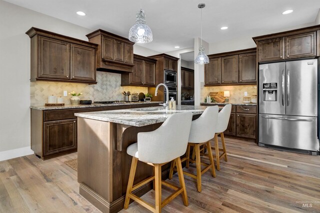 2043 E Lodge Trail Dr, Meridian, ID 83642 - kitchen featuring stainless steel appliances, light wood-type flooring, dark brown cabinetry, a breakfast bar, and decorative backsplash