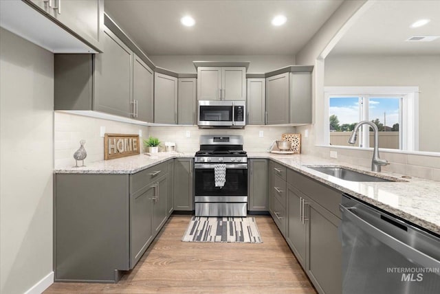 kitchen featuring light stone countertops, appliances with stainless steel finishes, gray cabinetry, sink, and light hardwood / wood-style floors