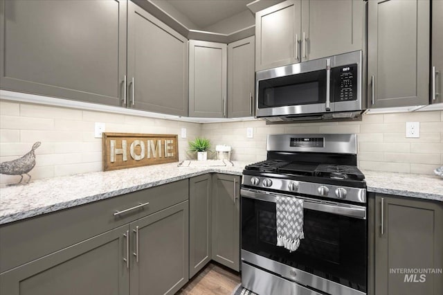 kitchen featuring gray cabinetry, light stone counters, backsplash, and appliances with stainless steel finishes