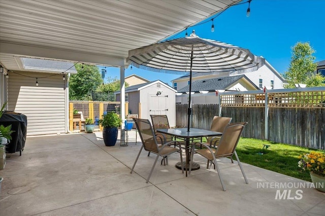 view of patio featuring outdoor dining area, an outdoor structure, a fenced backyard, and a storage unit