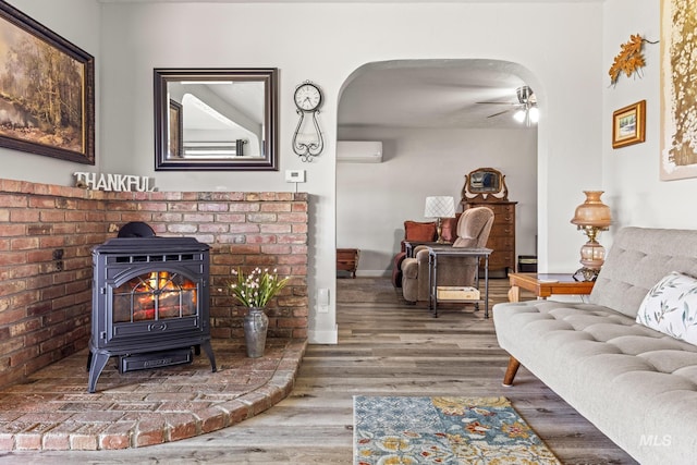 2208 Keithley Creek Rd, Midvale, ID 83645 - living area featuring an AC wall unit, a wood stove, wood finished floors, a ceiling fan, and arched walkways