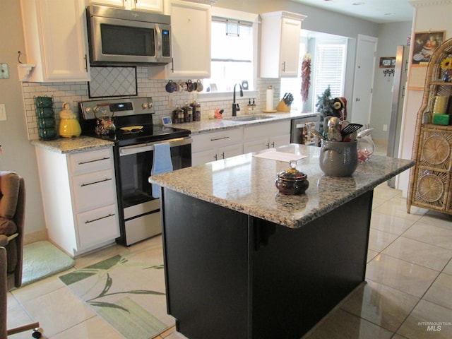 kitchen with light tile patterned floors, stainless steel appliances, a sink, white cabinetry, and backsplash