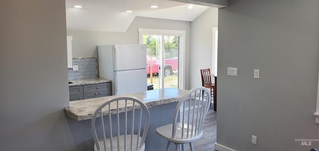 kitchen featuring tasteful backsplash, a breakfast bar, vaulted ceiling, gray cabinets, and white refrigerator