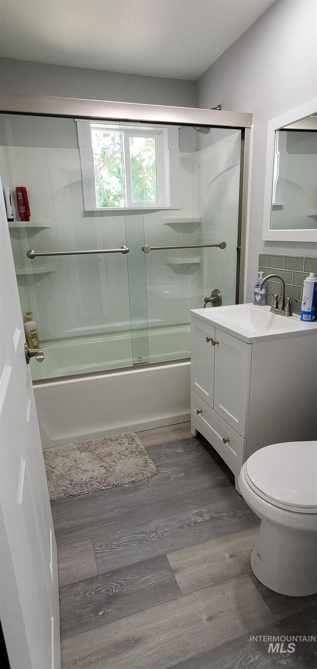 full bathroom with hardwood / wood-style flooring, toilet, bath / shower combo with glass door, vanity, and tasteful backsplash