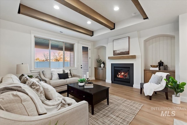 living room featuring light wood-type flooring, beamed ceiling, a glass covered fireplace, and recessed lighting