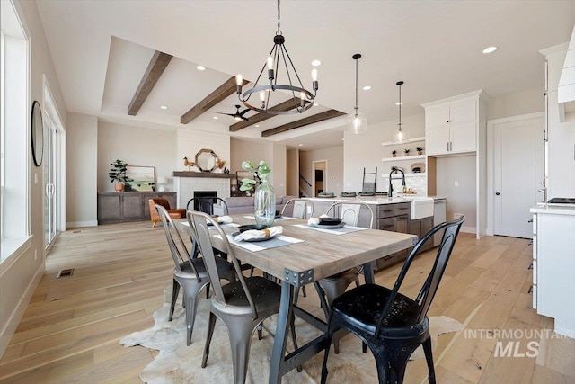 dining room with sink, a fireplace, beamed ceiling, light hardwood / wood-style floors, and a notable chandelier