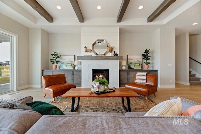 living room featuring a tiled fireplace, light hardwood / wood-style floors, and beamed ceiling