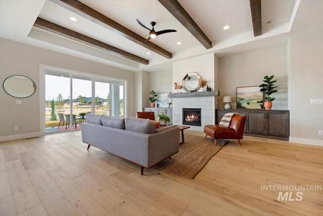 living room featuring a tile fireplace, light wood-type flooring, beam ceiling, and ceiling fan