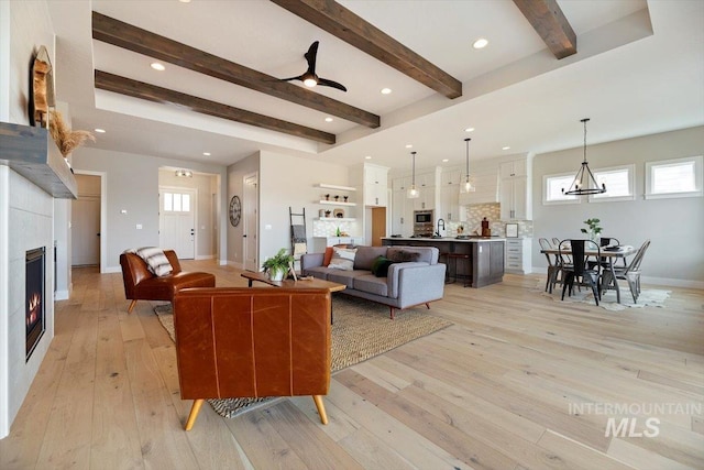 living room featuring ceiling fan, light hardwood / wood-style floors, and beamed ceiling