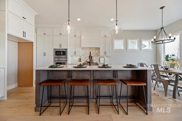 kitchen with decorative light fixtures, a large island, white cabinets, and appliances with stainless steel finishes