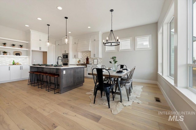 dining room with a notable chandelier, light hardwood / wood-style flooring, a wealth of natural light, and sink