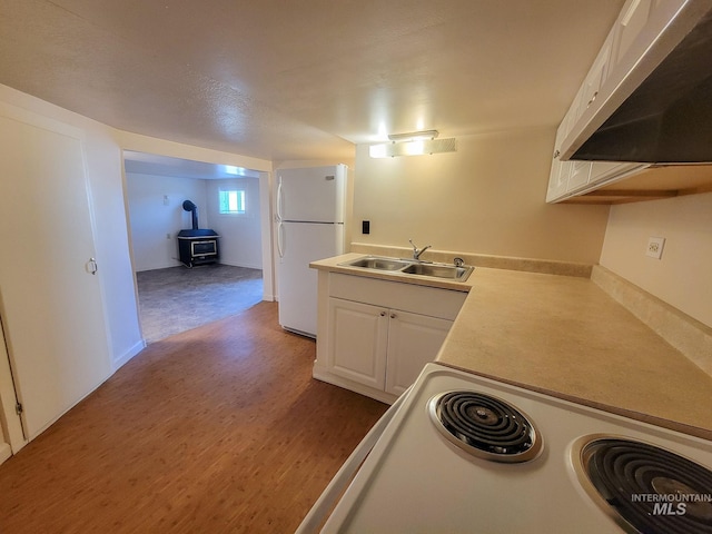 1603 11th Ave, Lewiston, ID 83501 - kitchen featuring freestanding refrigerator, a sink, under cabinet range hood, a wood stove, and white cabinetry