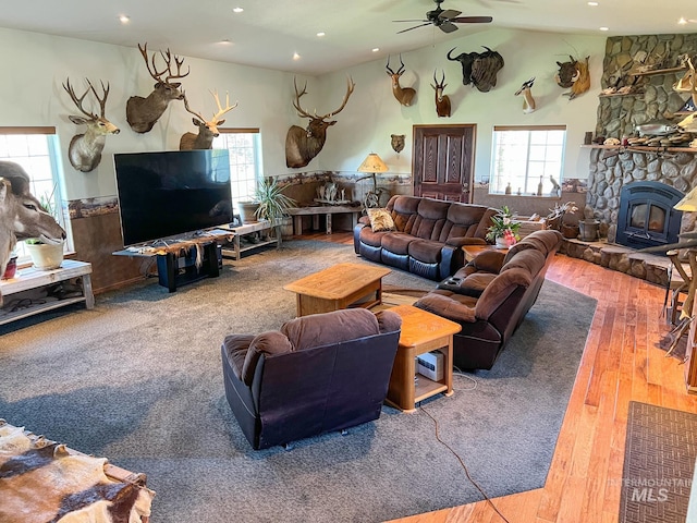 living room featuring hardwood / wood-style flooring, ceiling fan, a wood stove, and vaulted ceiling