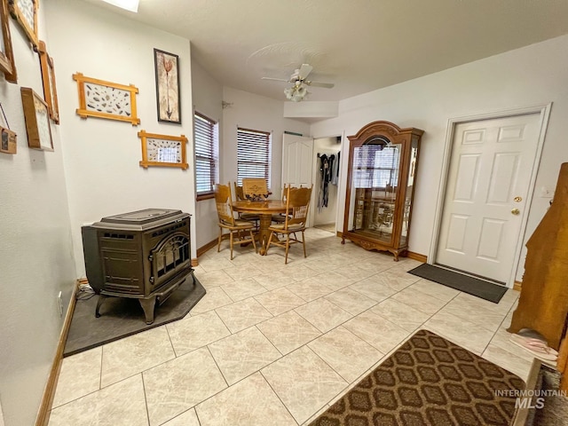 interior space with light tile patterned flooring, a wood stove, ceiling fan, and plenty of natural light