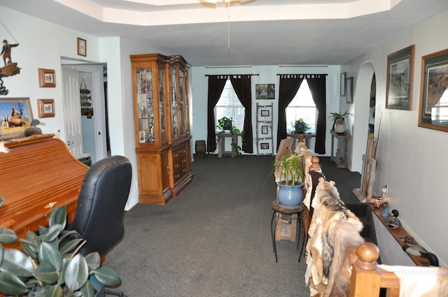 office area with a tray ceiling and dark carpet