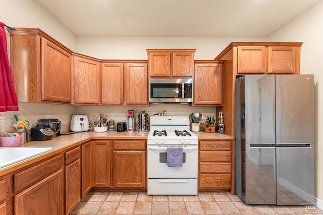 kitchen featuring appliances with stainless steel finishes, light countertops, light stone finish floors, and brown cabinetry