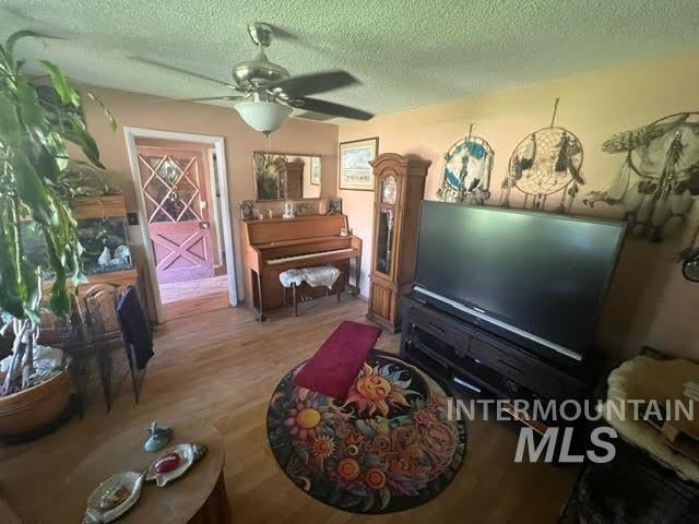 living room with ceiling fan, a textured ceiling, and hardwood / wood-style floors