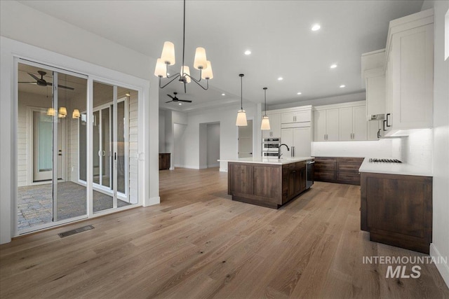 kitchen featuring backsplash, dark brown cabinets, a kitchen island with sink, pendant lighting, and white cabinetry