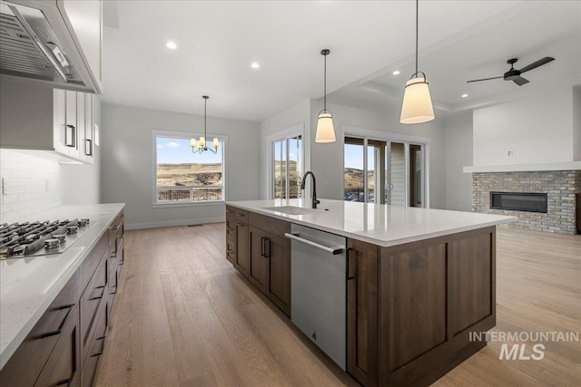 kitchen with wall chimney range hood, sink, decorative backsplash, a fireplace, and appliances with stainless steel finishes