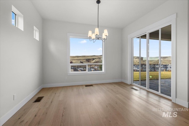 unfurnished dining area featuring a notable chandelier, light wood-type flooring, and plenty of natural light