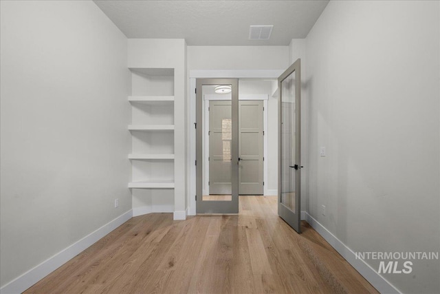 hallway with a textured ceiling, light hardwood / wood-style flooring, and french doors