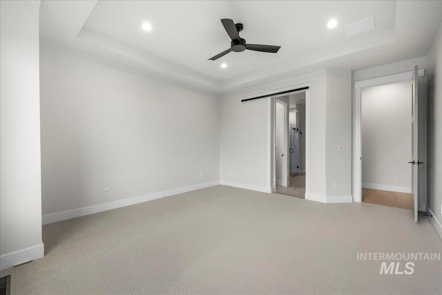 unfurnished bedroom with a tray ceiling, ceiling fan, a closet, and carpet