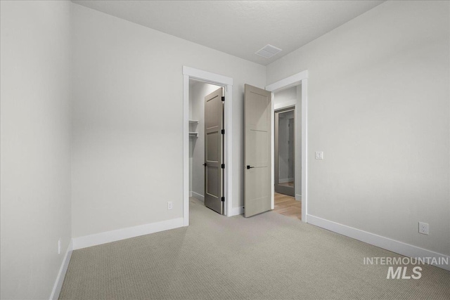 unfurnished bedroom featuring a spacious closet, a closet, and light colored carpet