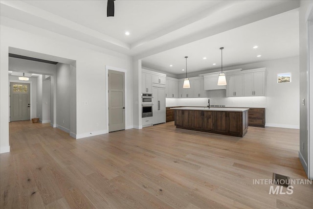 kitchen with a kitchen island with sink, white cabinets, light hardwood / wood-style flooring, tasteful backsplash, and dark brown cabinets